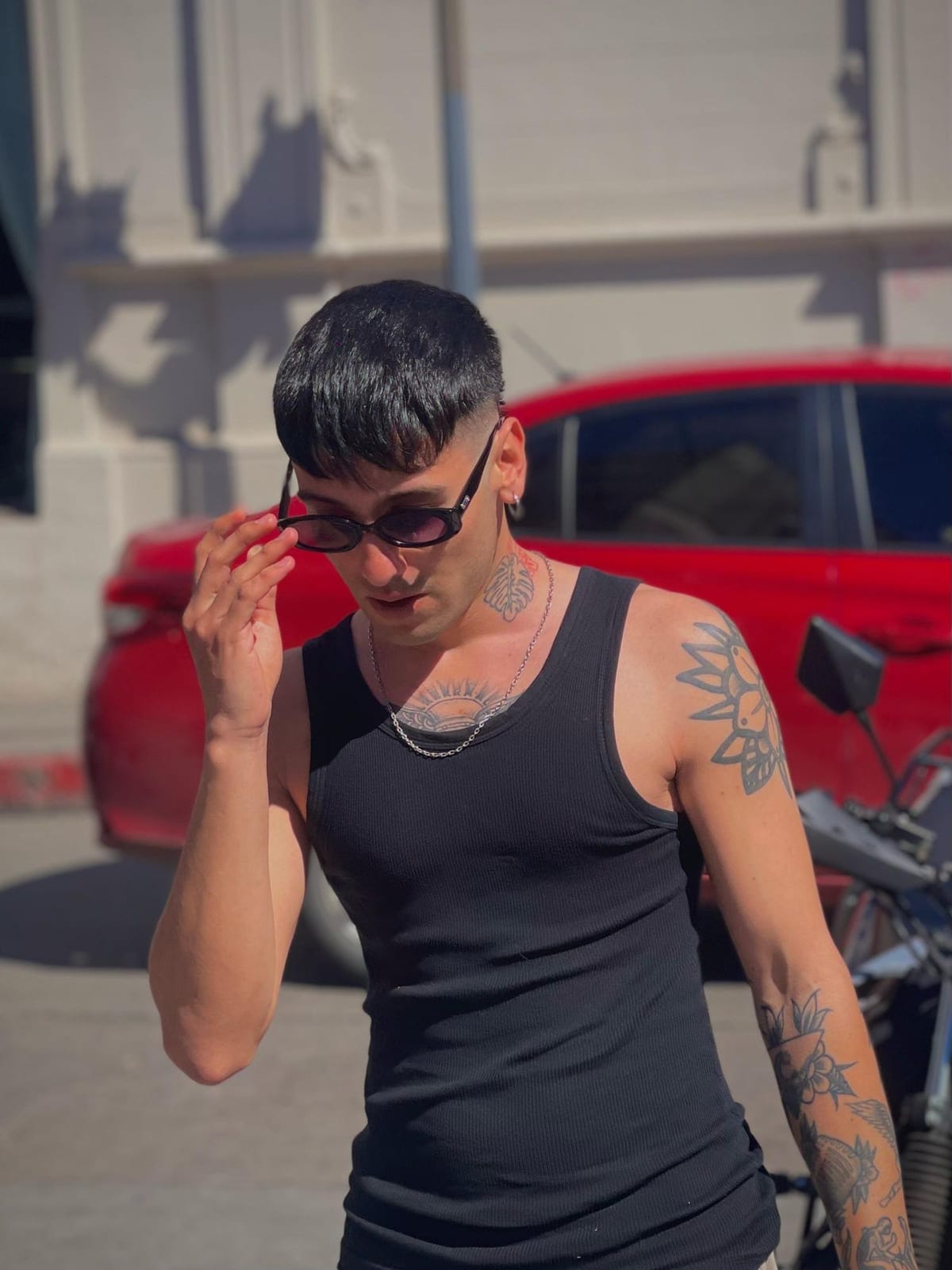 Misea acomodándose los anteojos, con un auto rojo detrás